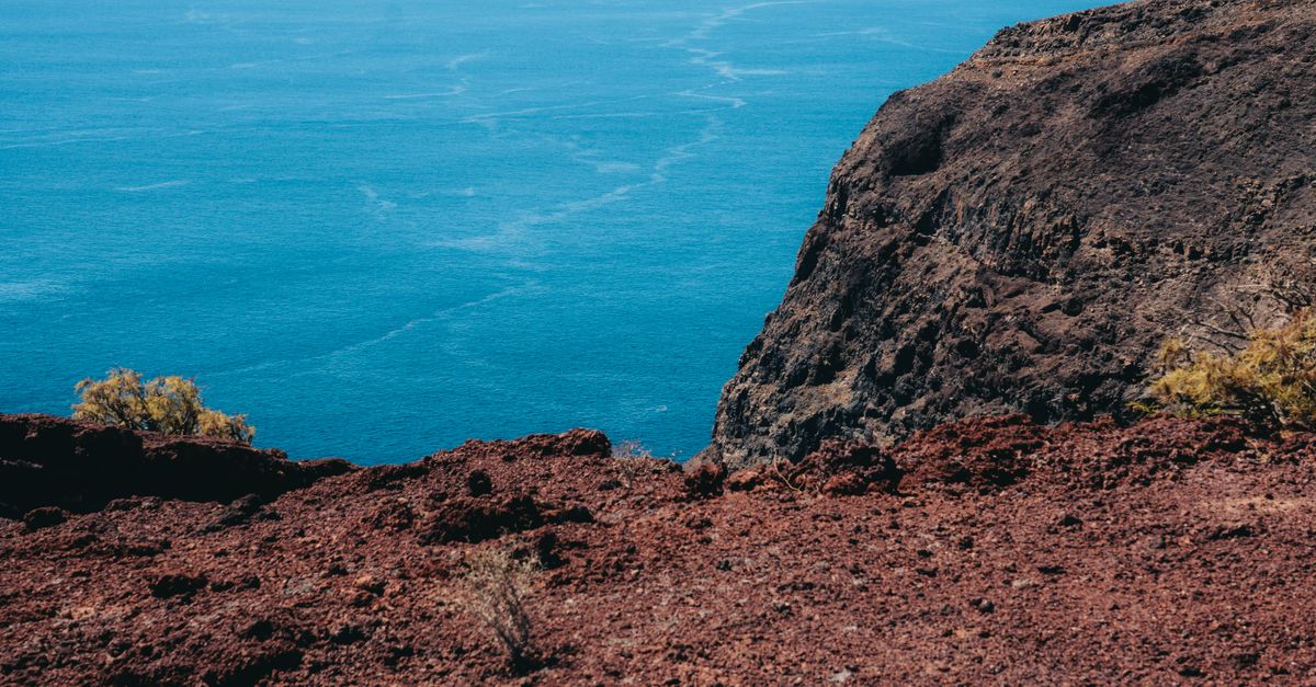 Red volcanic cliffs meeting the deep blue ocean in Alajeró, Canary Islands.