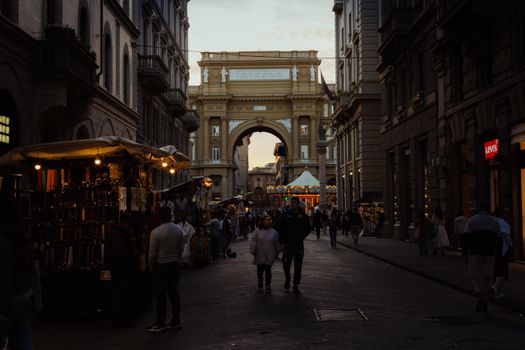 Bustling evening market at Piazza della Repubblica, Firenze with shoppers under the glowing lights.