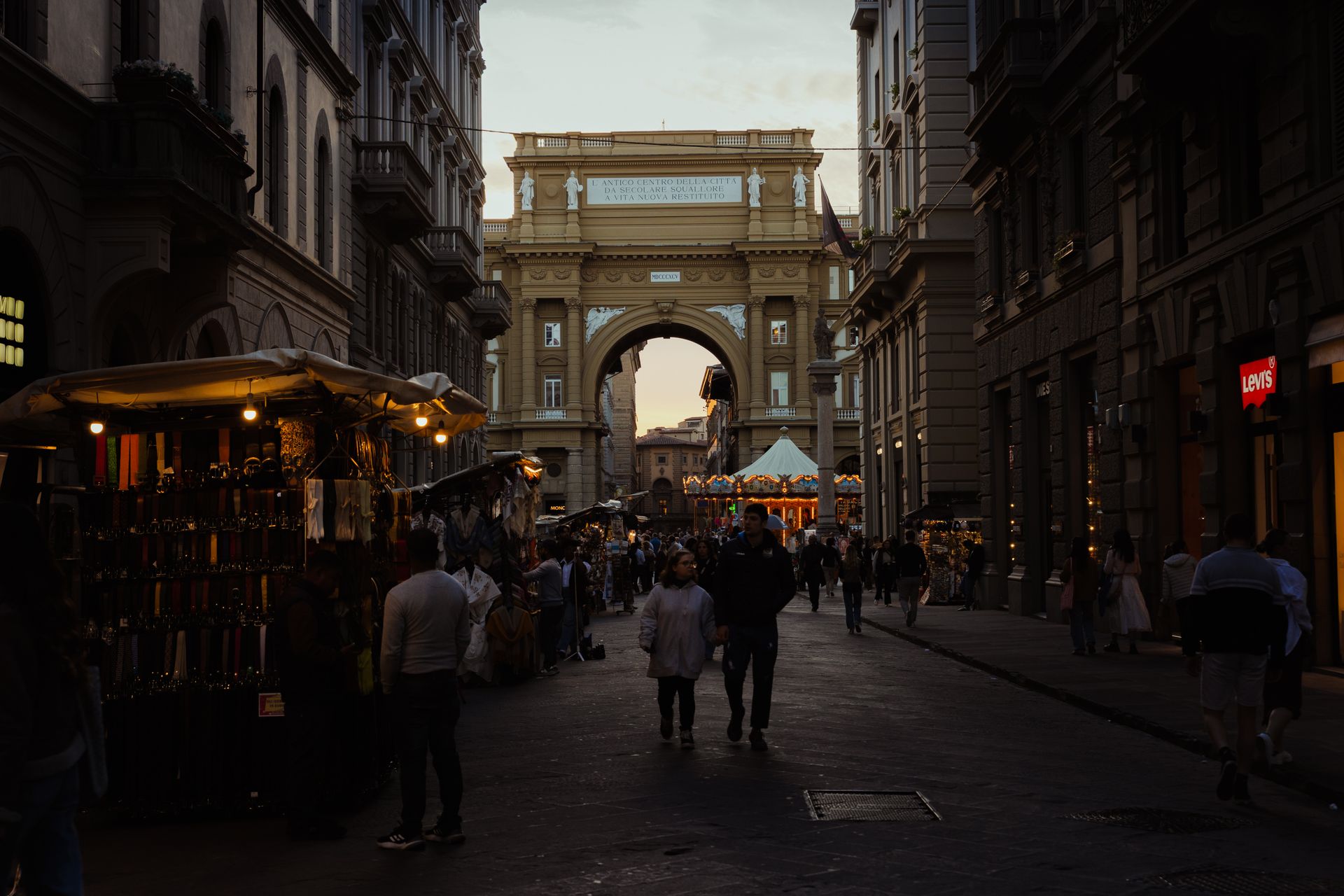 Bustling evening market at Piazza della Repubblica, Firenze with shoppers under the glowing lights.