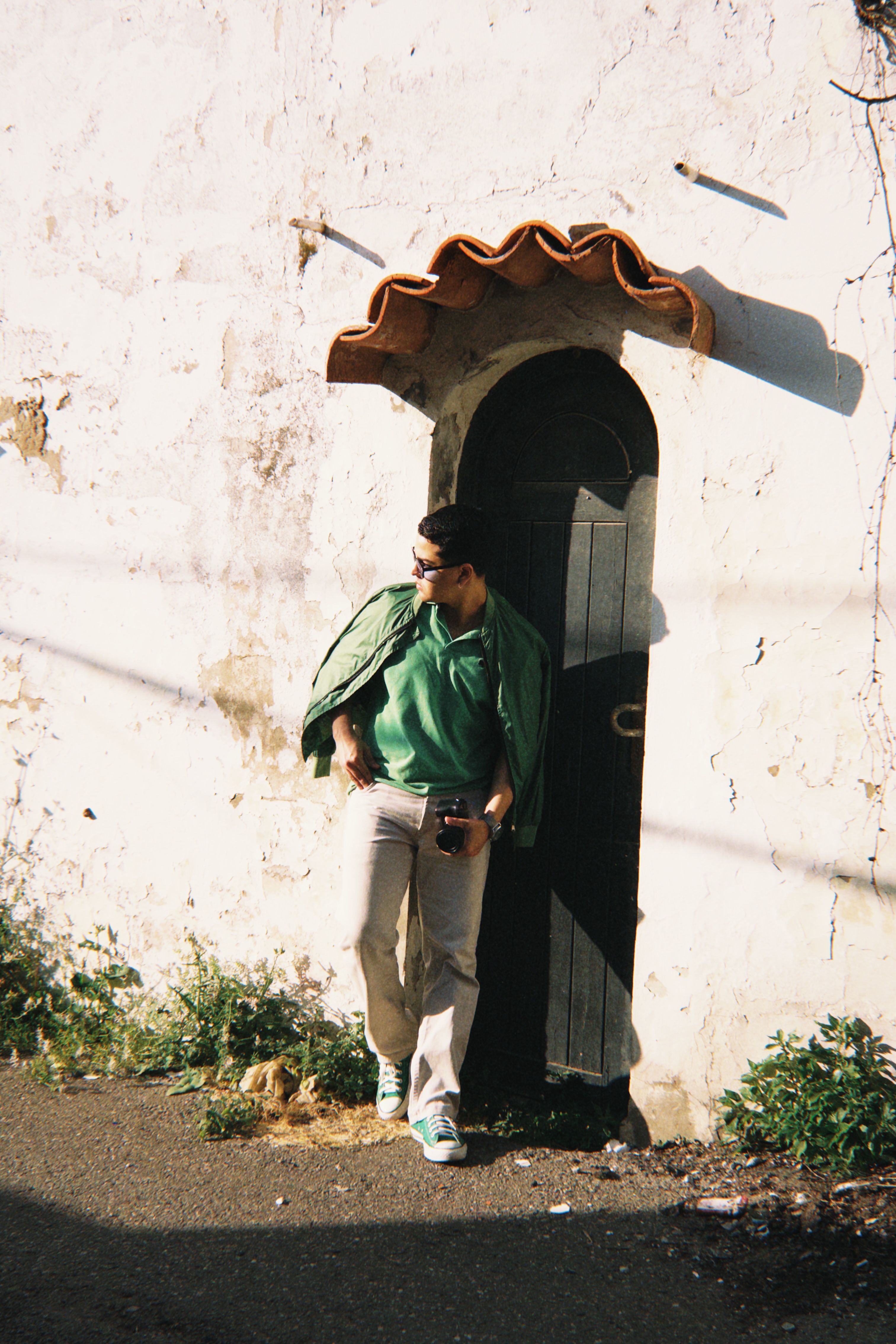 Man in green by rustic door, exuding casual urban style.
