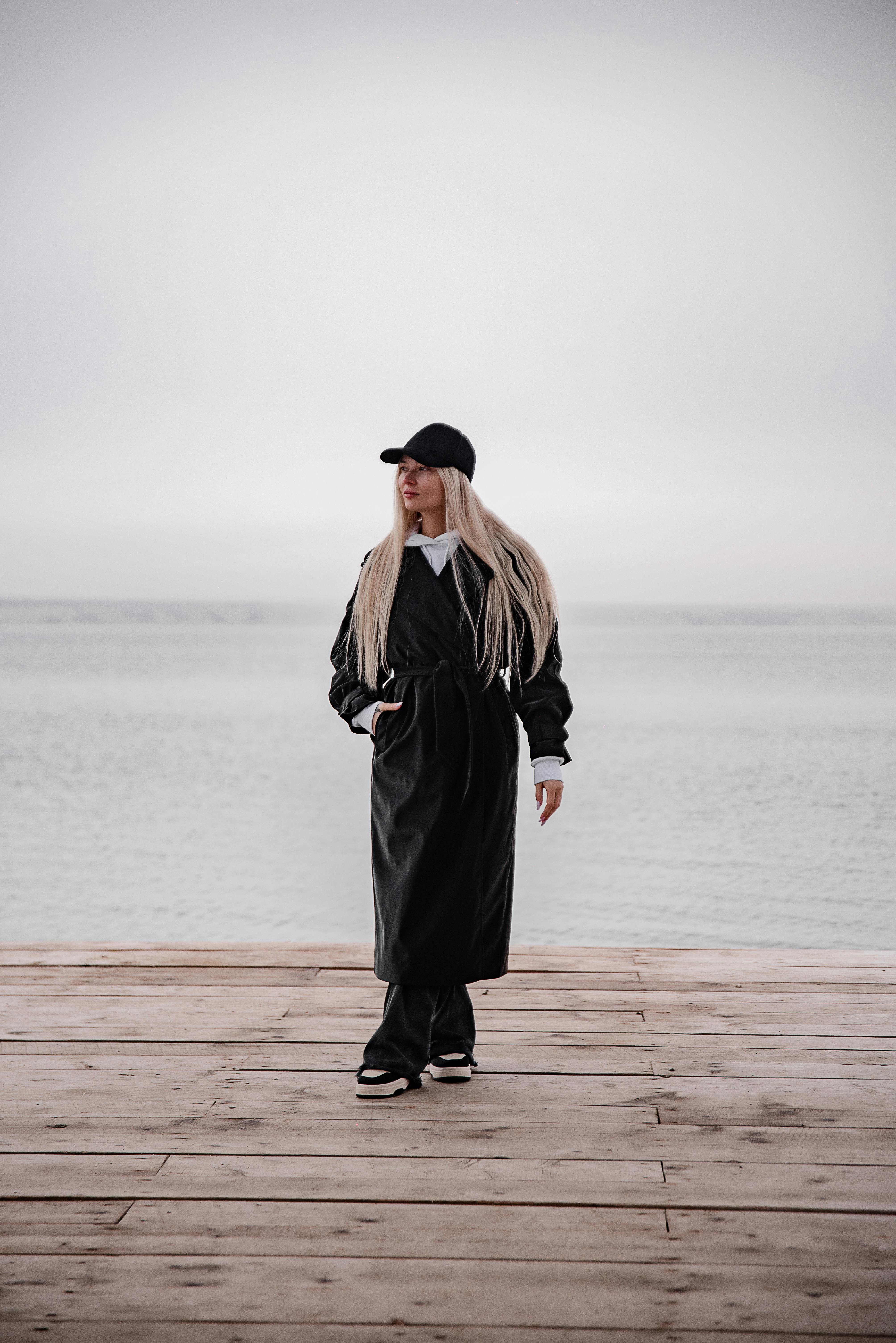 穿着黑色衣服的时髦女人走在木制码头上，背后是广阔的海洋背景