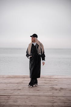 穿着黑色衣服的时髦女人走在木制码头上，背后是广阔的海洋背景