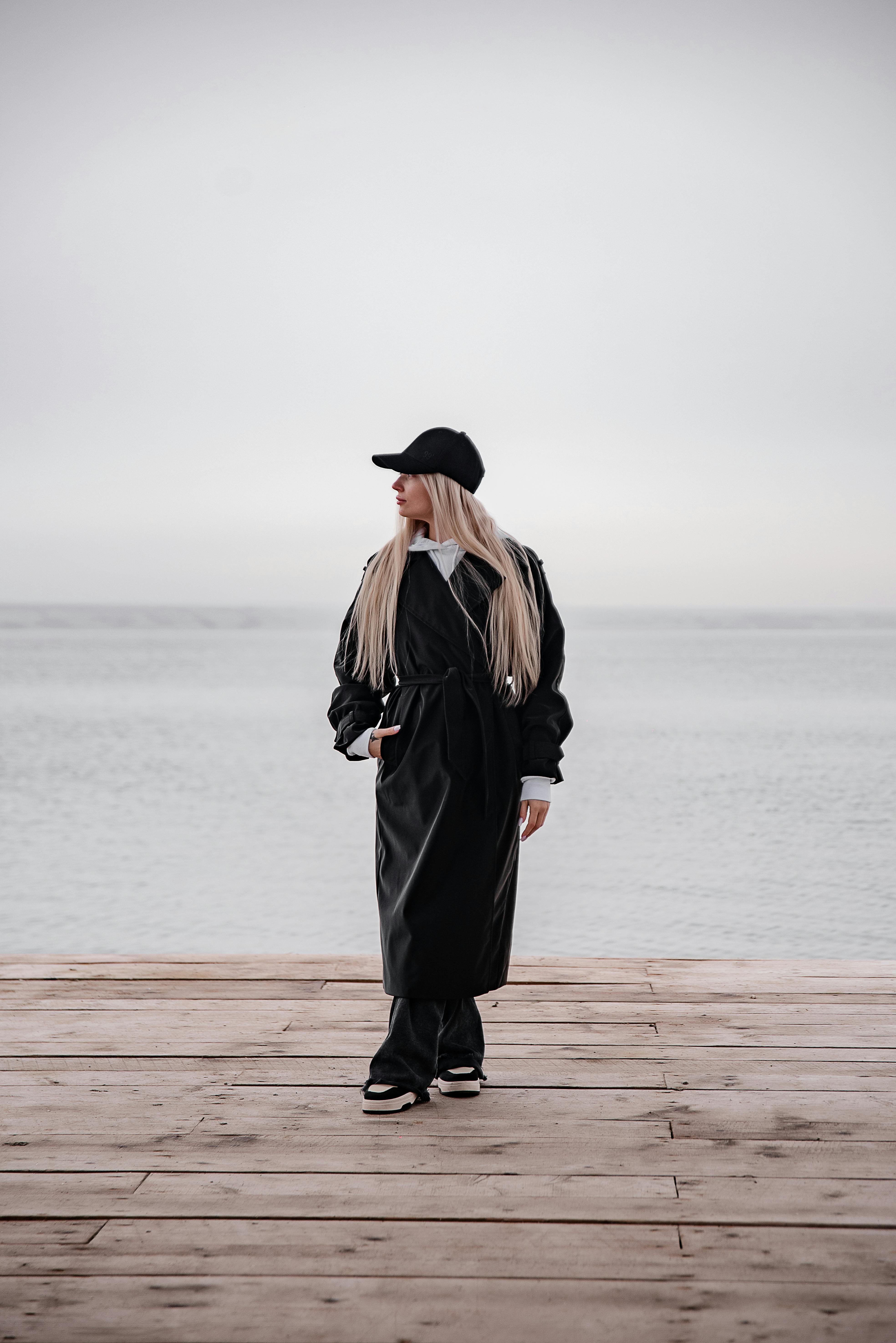 穿着黑色服装的时尚女子站在码头上，俯瞰着平静的大海
