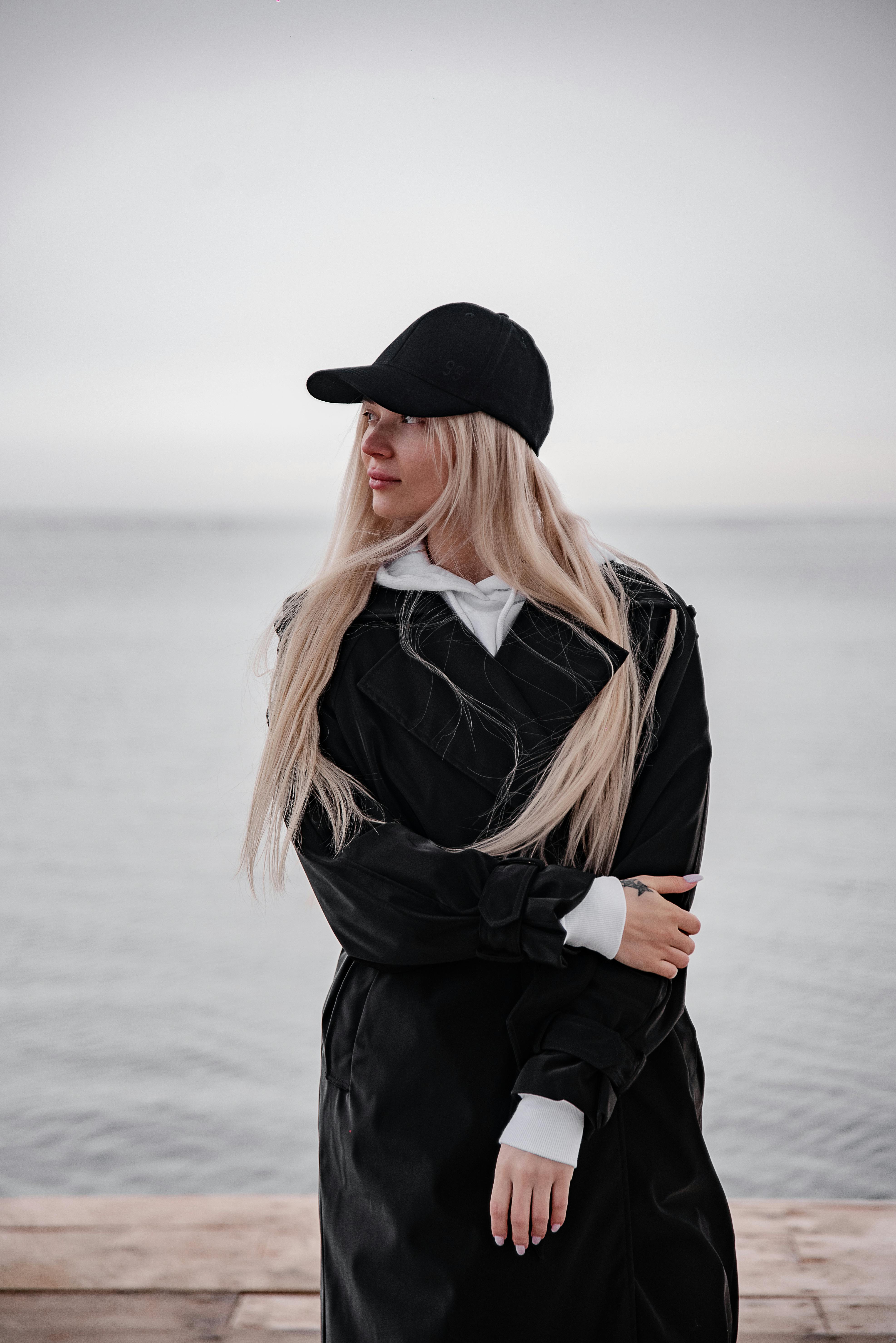 穿着黑色外套和帽子的时尚女人站在海边，拥抱宁静的时刻