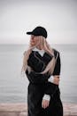 穿着黑色外套和帽子的时尚女人站在海边，拥抱宁静的时刻