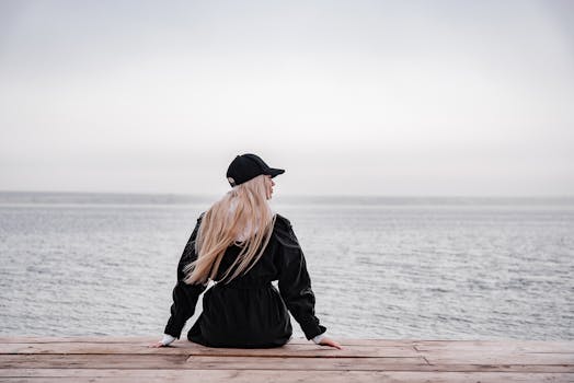 一名女子坐在码头上，凝视着大海，营造出一幅宁静的海岸风景