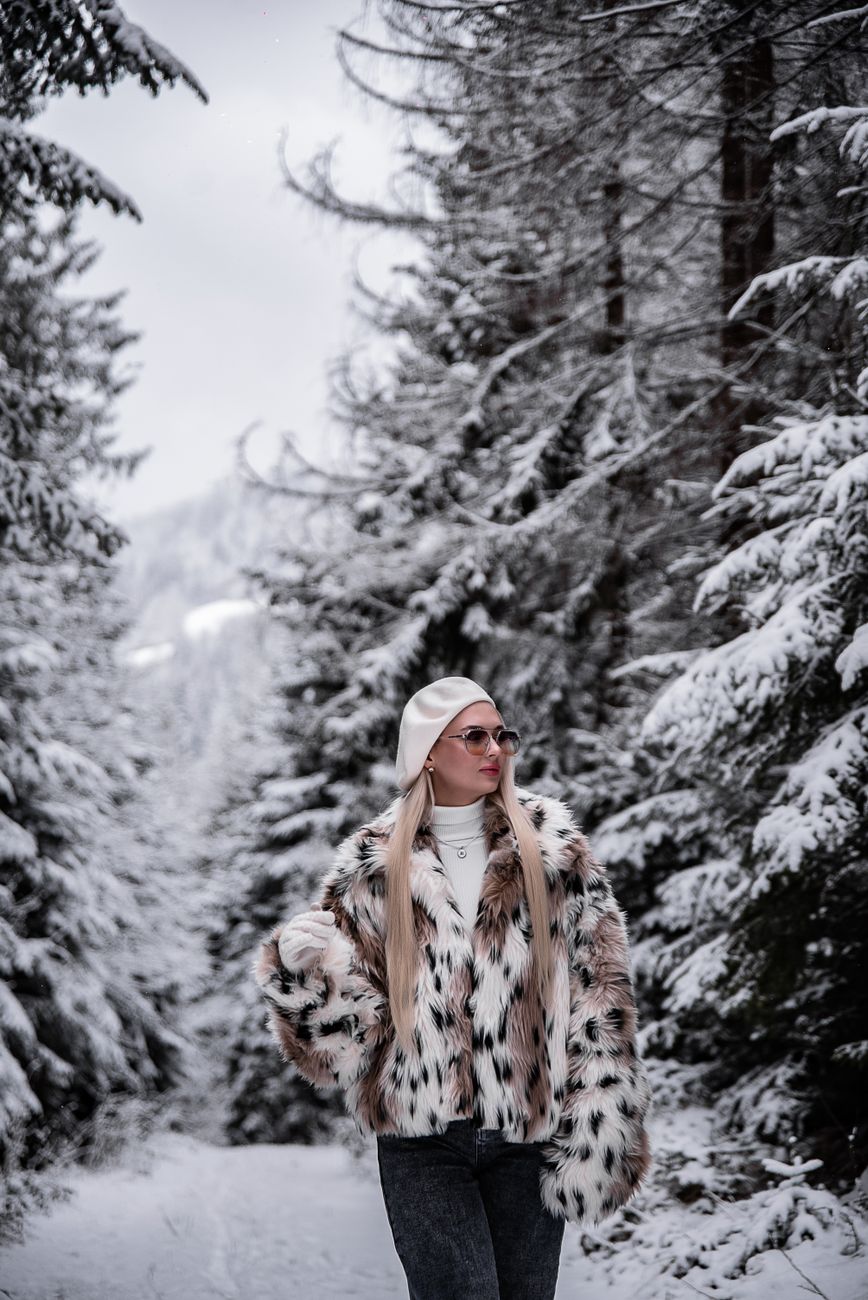Uma mulher elegante com um casaco de pele caminha por uma floresta nevada durante o inverno.