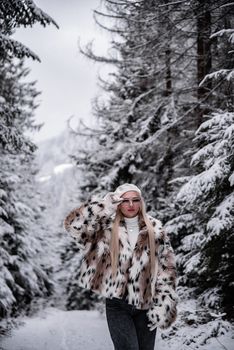 Stylish woman in faux fur coat exploring a snowy forest landscape, embodying winter fashion.