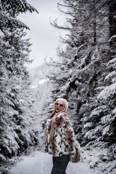 Stylish woman in faux fur coat in snowy forest, epitomizing winter fashion.