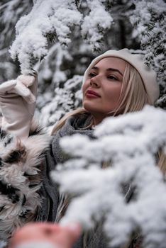 A young woman in winter clothing enjoys a snowy day outdoors, surrounded by snow-covered branches.