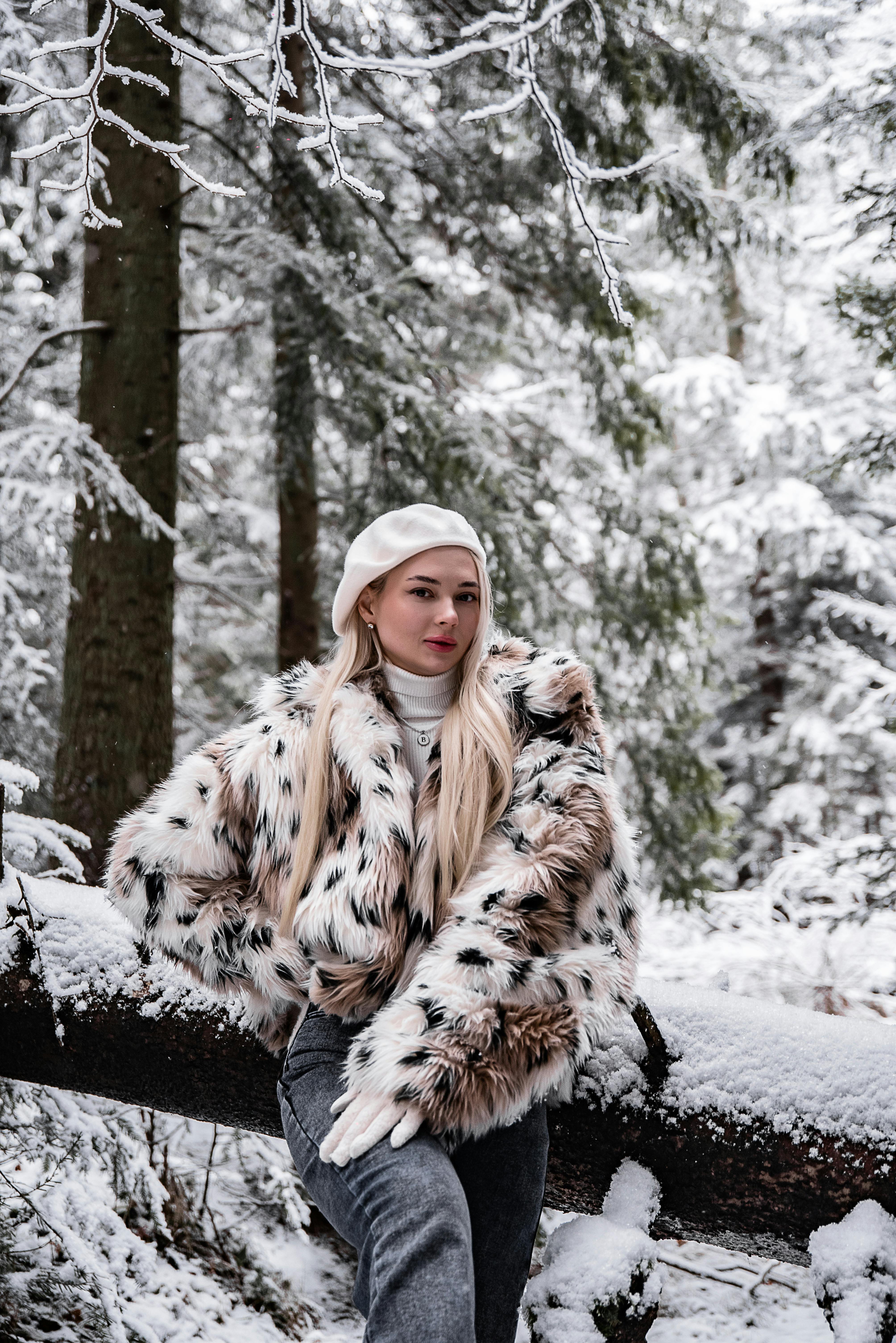 穿着时尚毛皮大衣的女人站在白雪皑皑的森林场景中