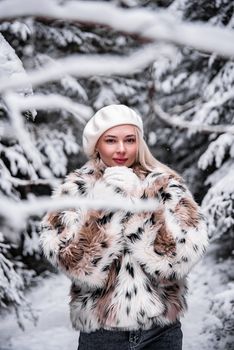 Stylish blonde woman wearing a fur coat and beret in a snowy forest. Fashionable winter scene.