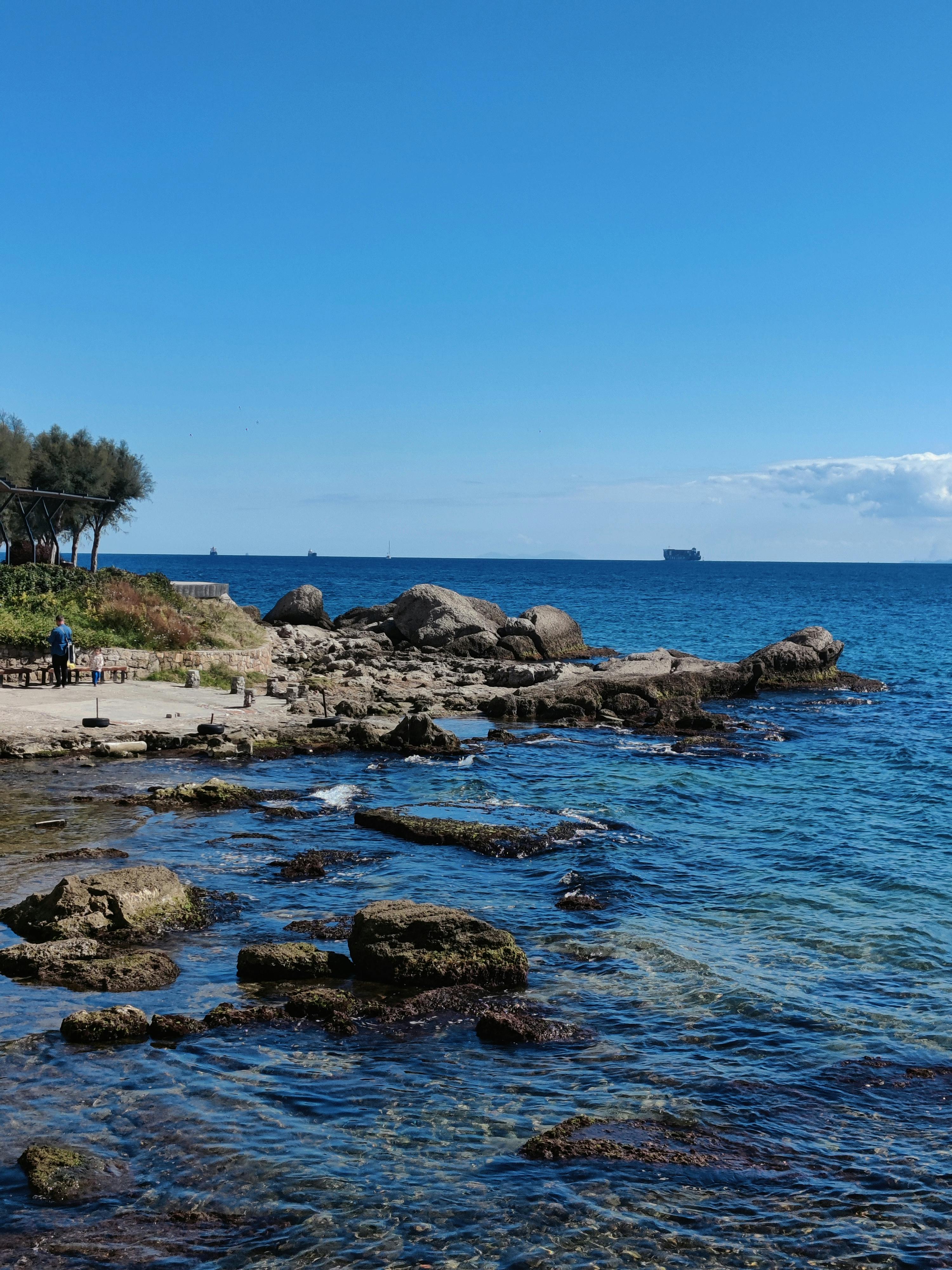 宁静的海滨景观，岩石海岸、清澈蔚蓝的海水和地平线上的船只
