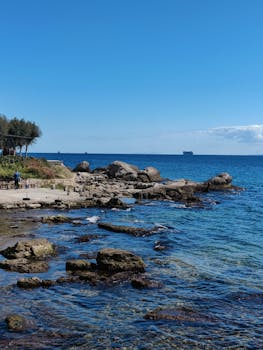 宁静的海滨景观，岩石海岸、清澈蔚蓝的海水和地平线上的船只