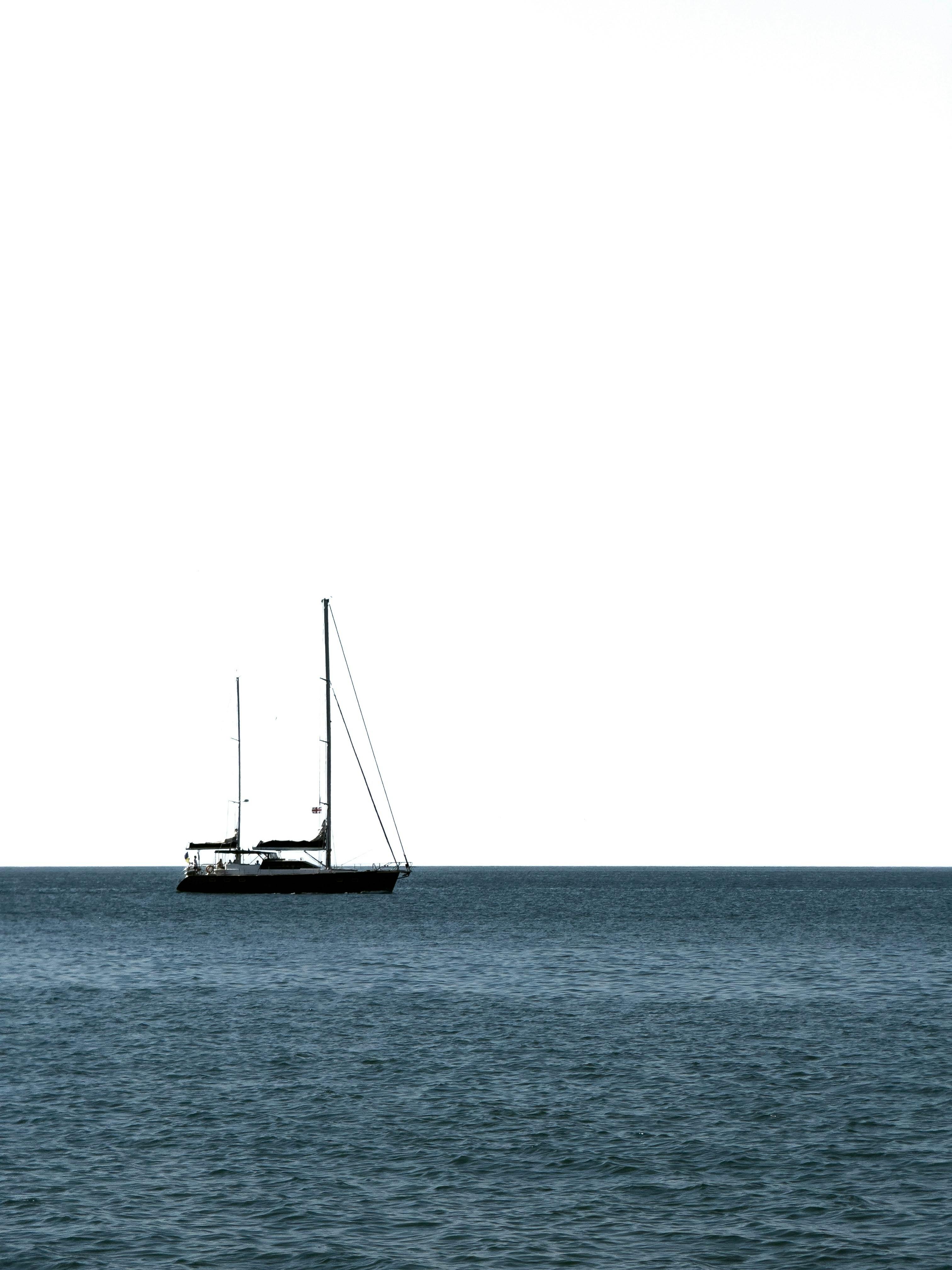 一艘孤独的帆船在平静的海面上，映衬着广阔晴朗的天空，传达着孤独与和平