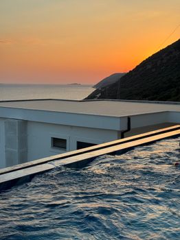 Infinity pool reflecting sunset with ocean view and modern architecture.