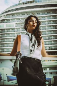 Stylish woman with scarf poses in front of luxury cruise ship, exuding elegance and adventure.