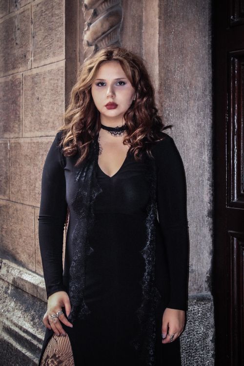 Free A woman dressed in gothic style, posing against a stone wall, exuding elegance and mystery. Stock Photo