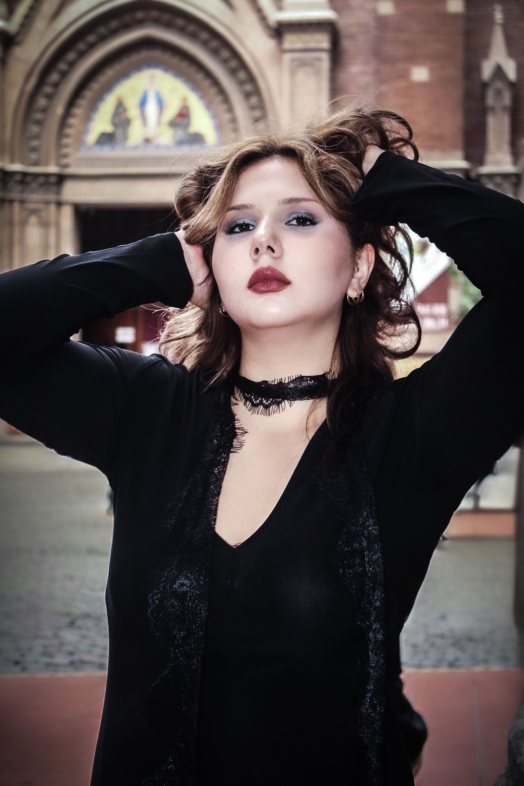 A fashionable woman poses confidently in front of an ornate historic building's entrance.