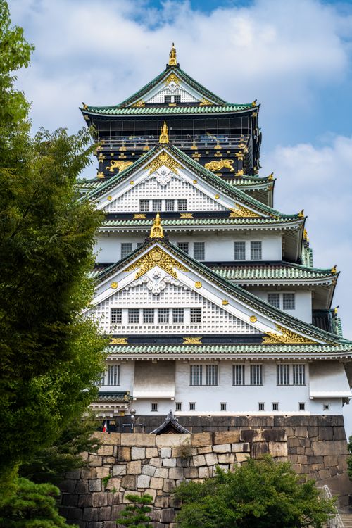 Free Beautiful architectural details of Osaka Castle surrounded by lush greenery under a bright blue sky. Stock Photo