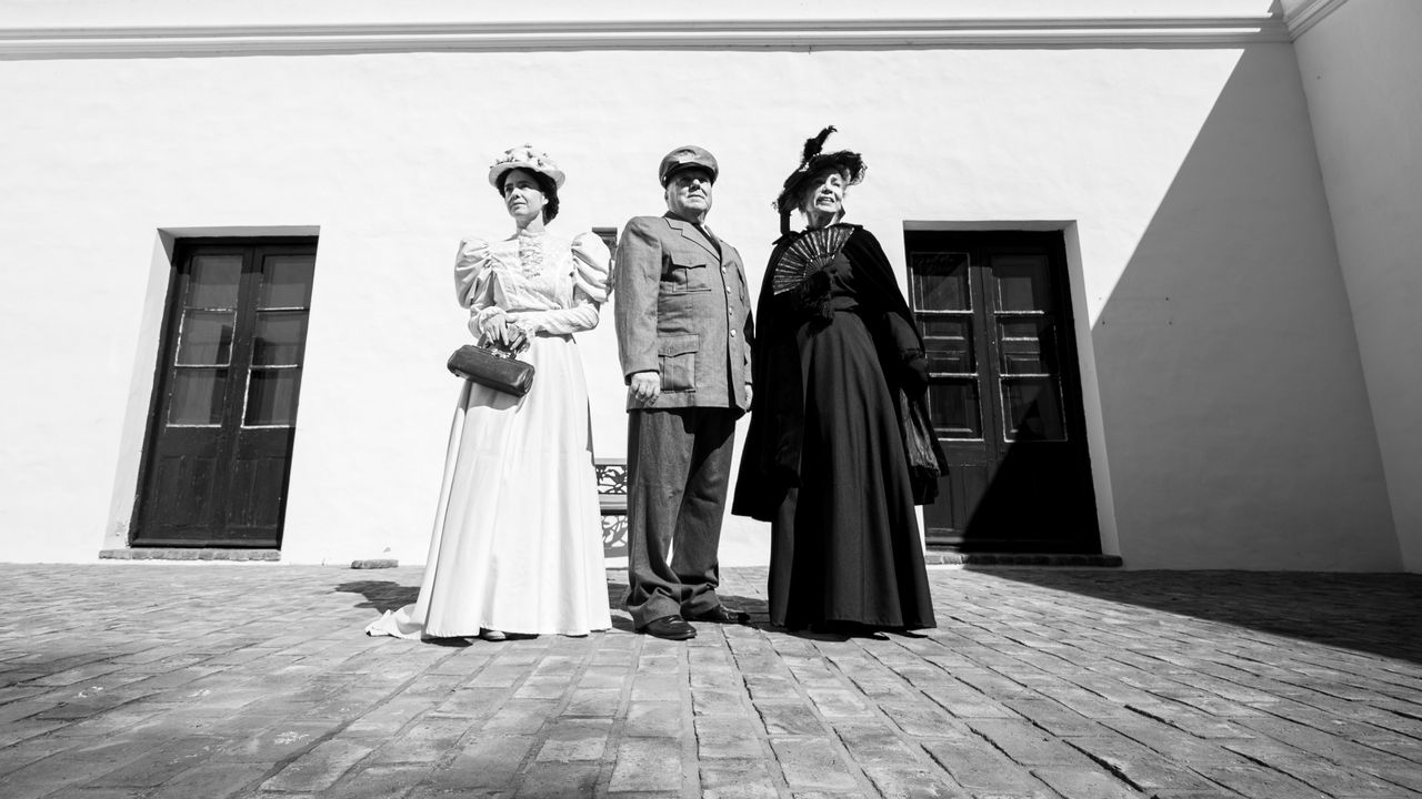 black and white photo of three adults in vintage costumes posed outdoo