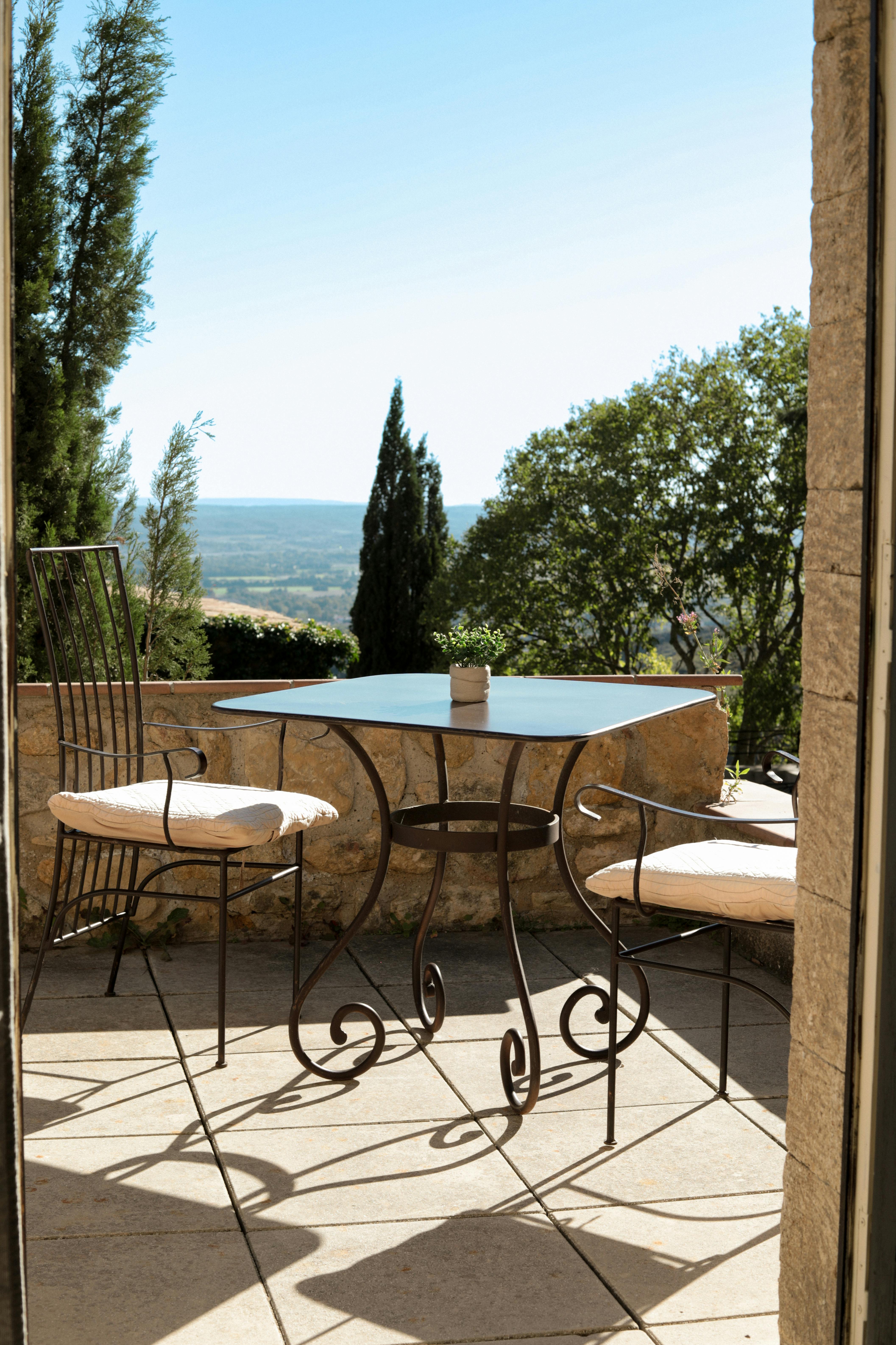 Sunlit terrace with wrought iron furniture overlooking Provence landscape.