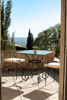 Sunlit terrace with wrought iron furniture overlooking Provence landscape.