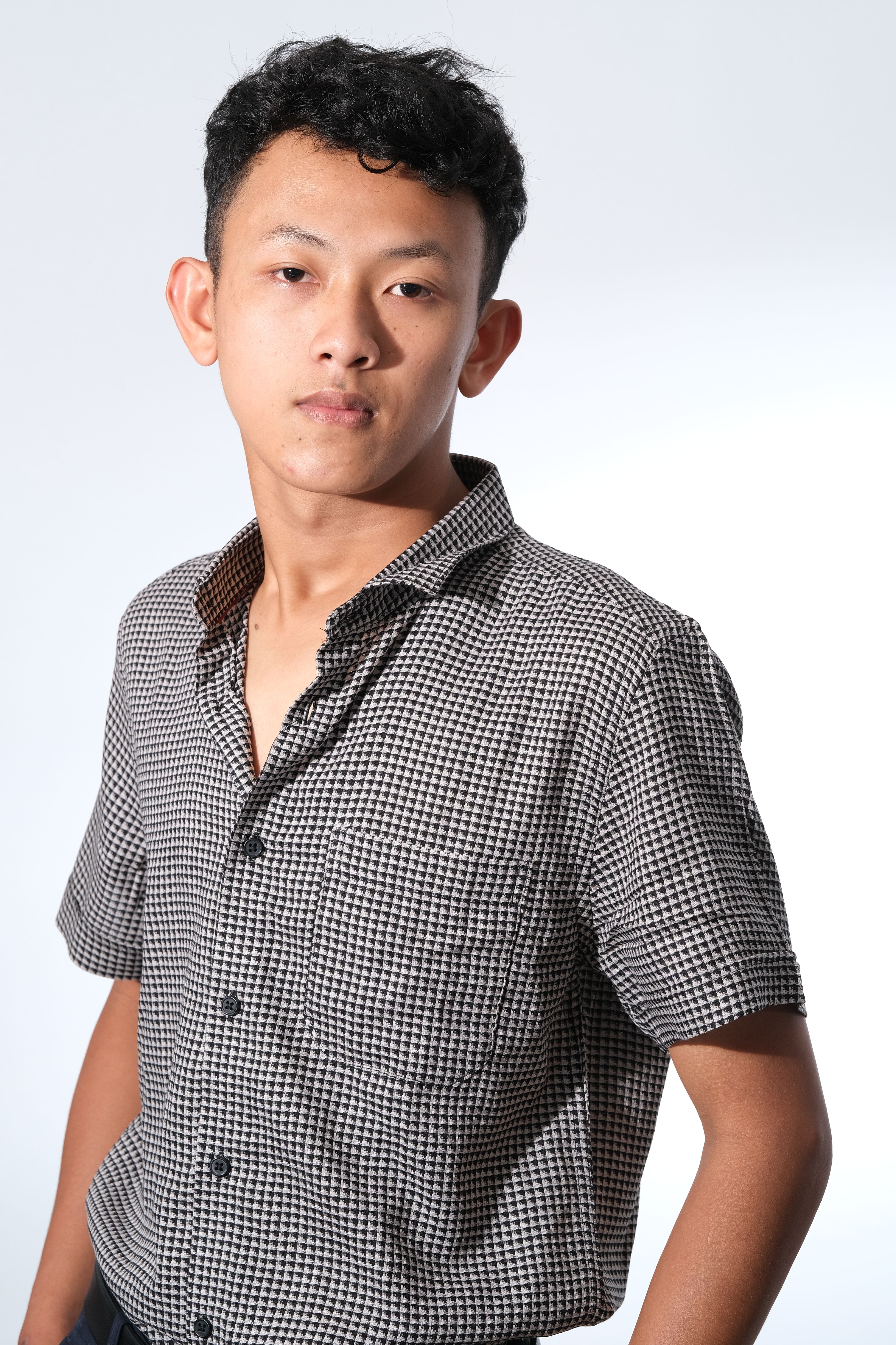 Studio portrait of a young adult male wearing a checkered shirt, captured with a bright and modern style.