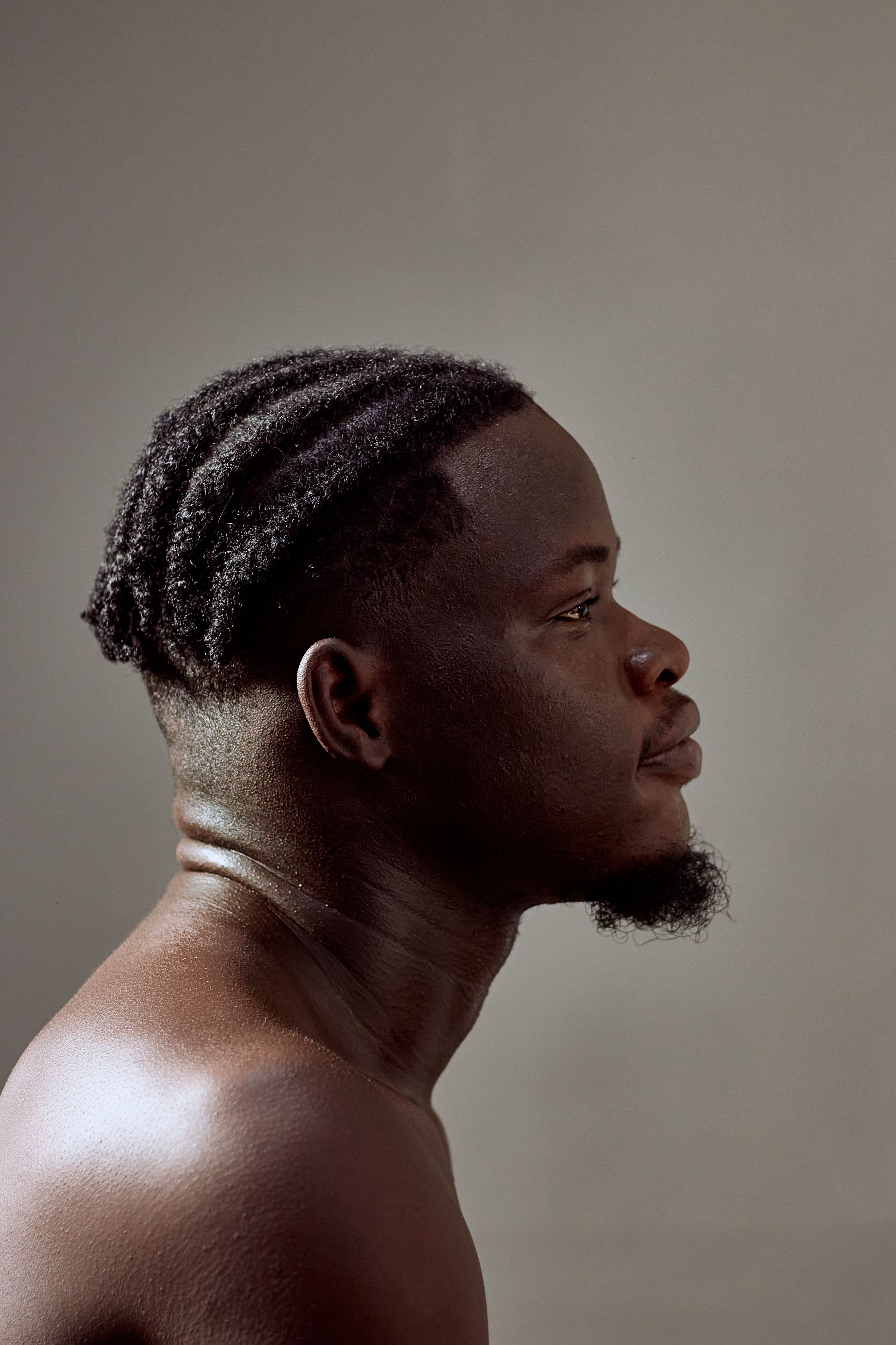 Profile portrait of a young black man with braided hair and neutral background.