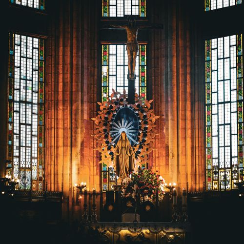 Free A beautiful church interior featuring stained glass windows, religious statues, and candlelit atmosphere. Stock Photo