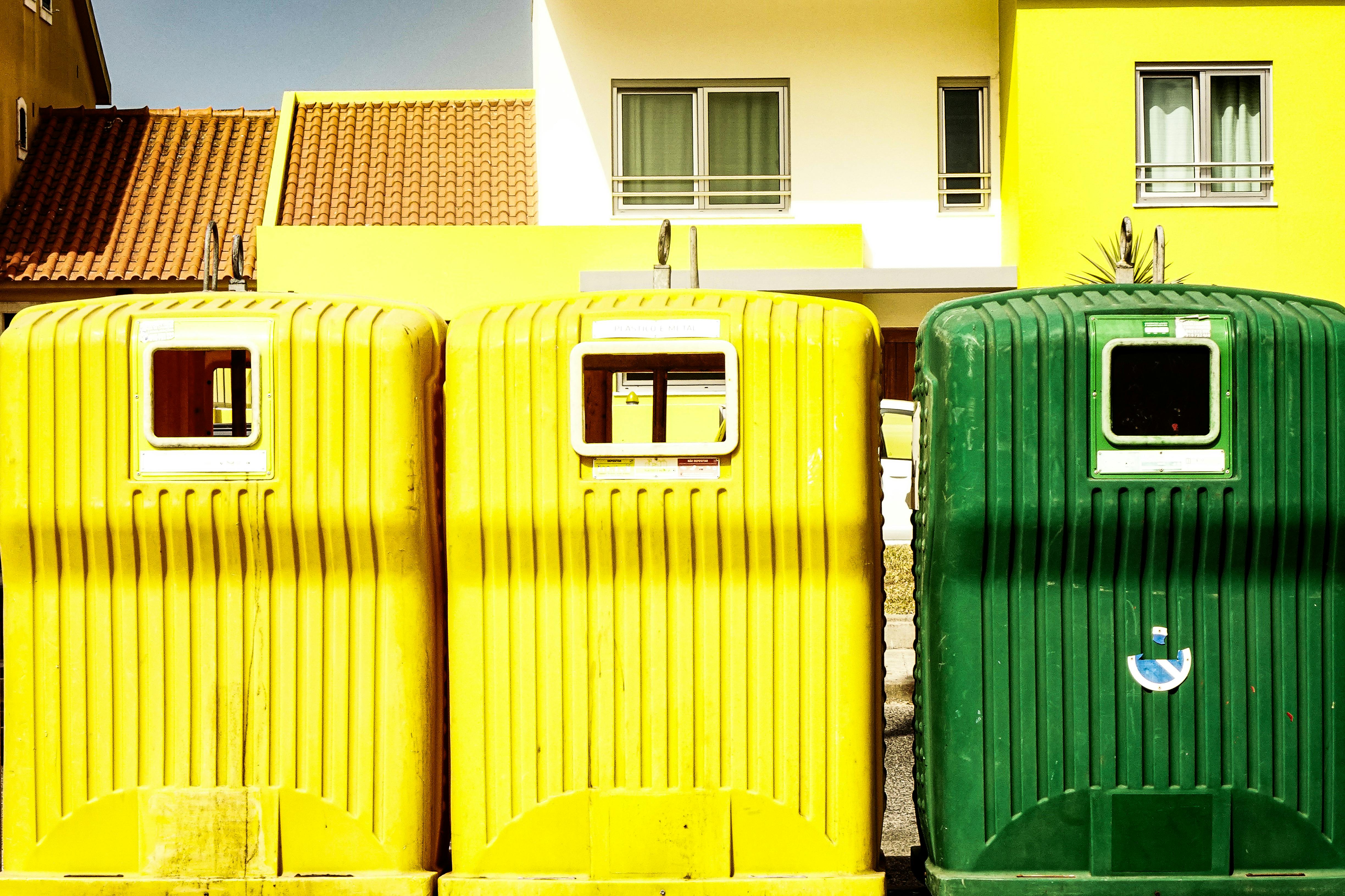 Colorful recycling bins stand in front of a sunny, modern residential building, showcasing urban sustainability.