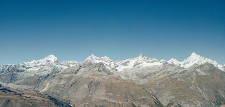 Stunning aerial view of the snow-capped Swiss Alps in Zermatt, capturing the majestic range under a clear blue sky.