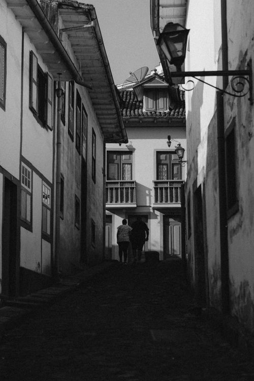 Free Black and white photo of a narrow alley with two people walking amidst historical buildings. Stock Photo