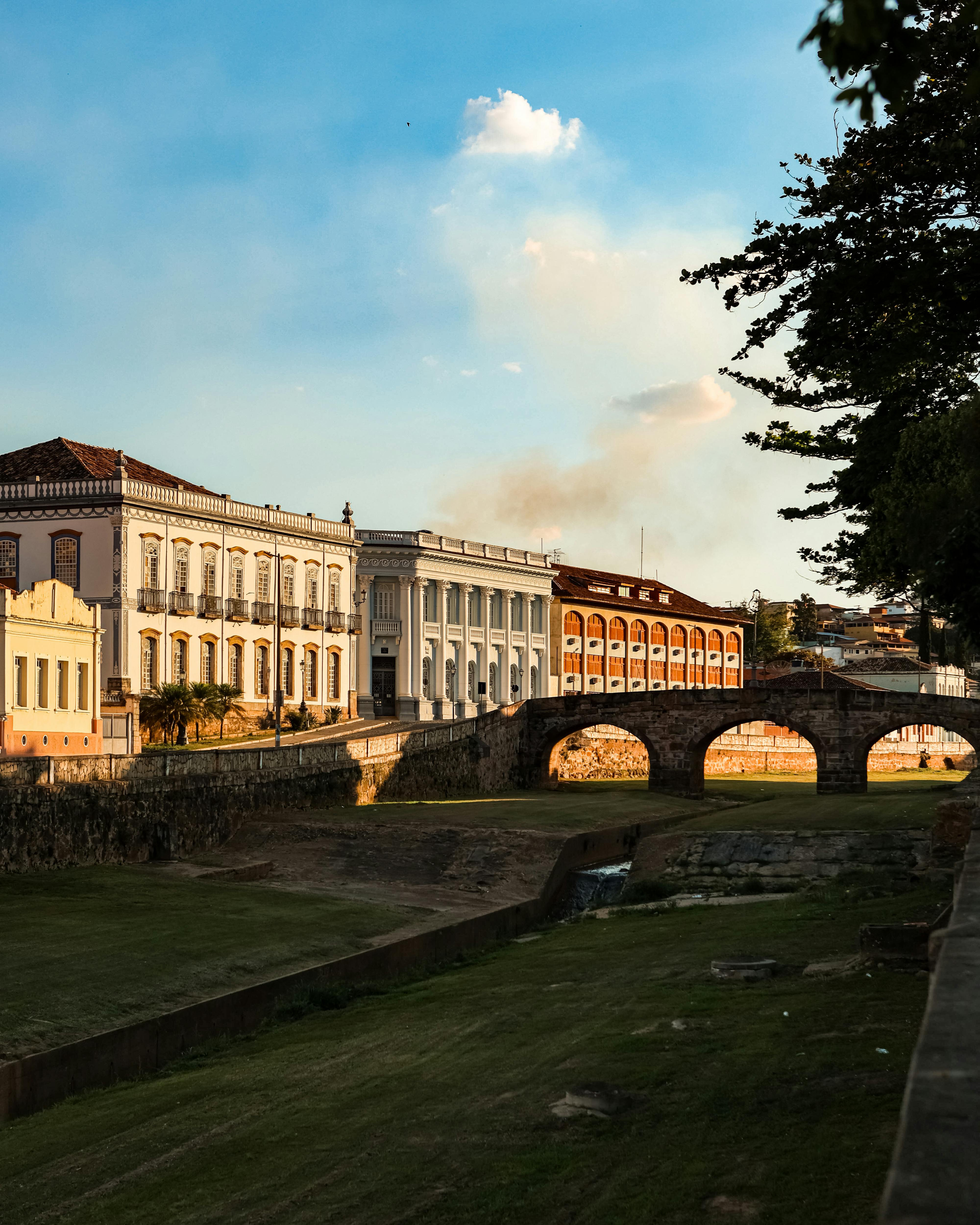 古老的殖民建筑旁，宁静的景色中，夕阳的温暖光芒洒在一座石桥上