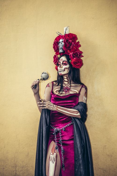 Free Woman in elaborate Day of the Dead attire with red roses and skull makeup against a yellow background. Stock Photo