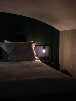 Comfortable bedroom with soft lighting and cozy atmosphere, featuring a bed and a lit bedside lamp.