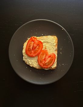Simple toast with creamy spread and fresh tomatoes on a dark plate.