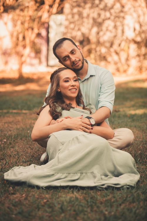 Free A couple enjoying a sunny day outdoors, sitting on grass with a romantic vibe. Stock Photo