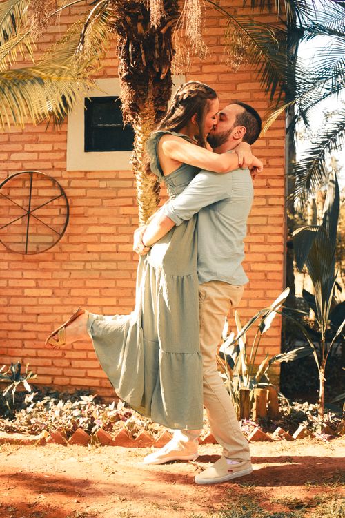 Free A loving couple shares a joyful embrace outside a brick house under sunlight. Stock Photo