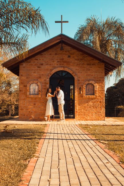 Fotomural Una pareja frente a una capilla de ladrillo rústica bajo palmeras durante el atardecer.