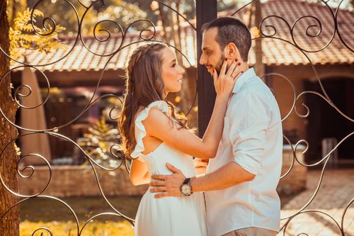 Free A couple sharing an intimate moment outdoors with a beautiful gate backdrop, captured in warm tones. Stock Photo