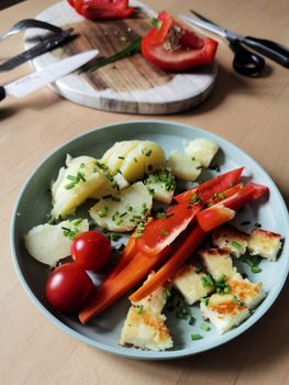 A vibrant plate featuring potatoes, cherry tomatoes, red peppers, and grilled cheese on a wooden table.
