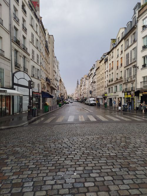 Free A serene view of a Paris street with wet cobblestones after rainfall, lined with classic buildings. Stock Photo