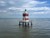 红白相间的灯塔矗立在平静的蓝色大海中，其头顶散布着朵朵云彩