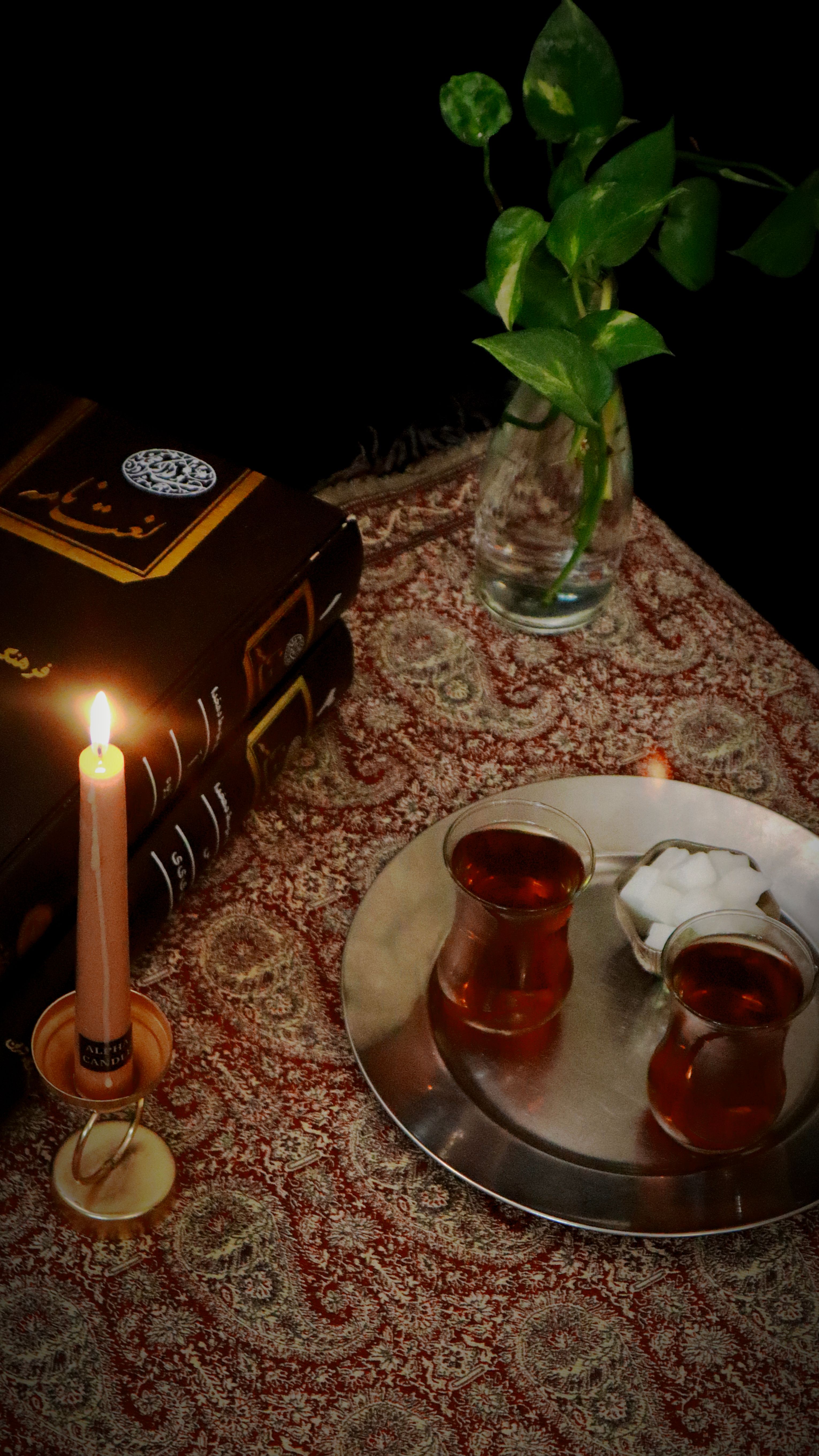 A cozy traditional setting with tea, books, and candlelight on a patterned fabric.