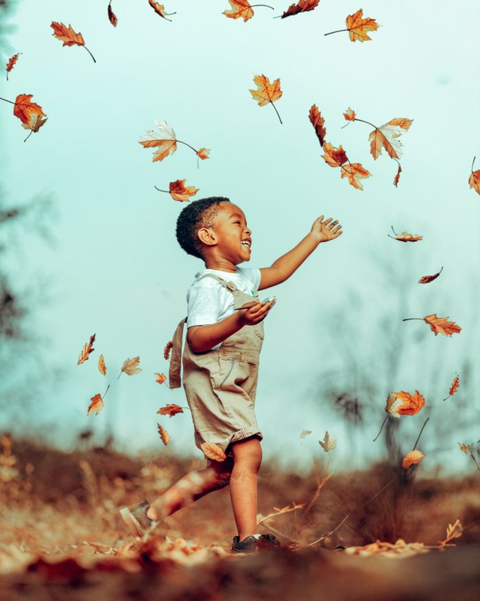 A child playing happily among falling autumn leaves