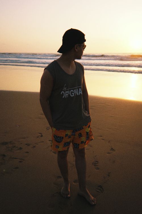 Free Silhouetted young man stands on a sandy beach, watching the sunset over the ocean. Stock Photo
