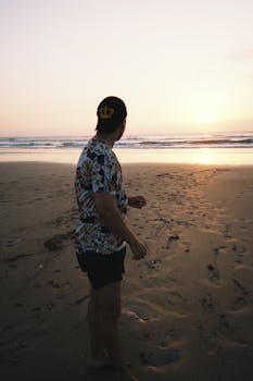 一名男子站在海滩上，观看日落，捕捉到地平线的宁静之美