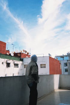 一个人站在屋顶上俯瞰城市，映衬着云朵和蓝天