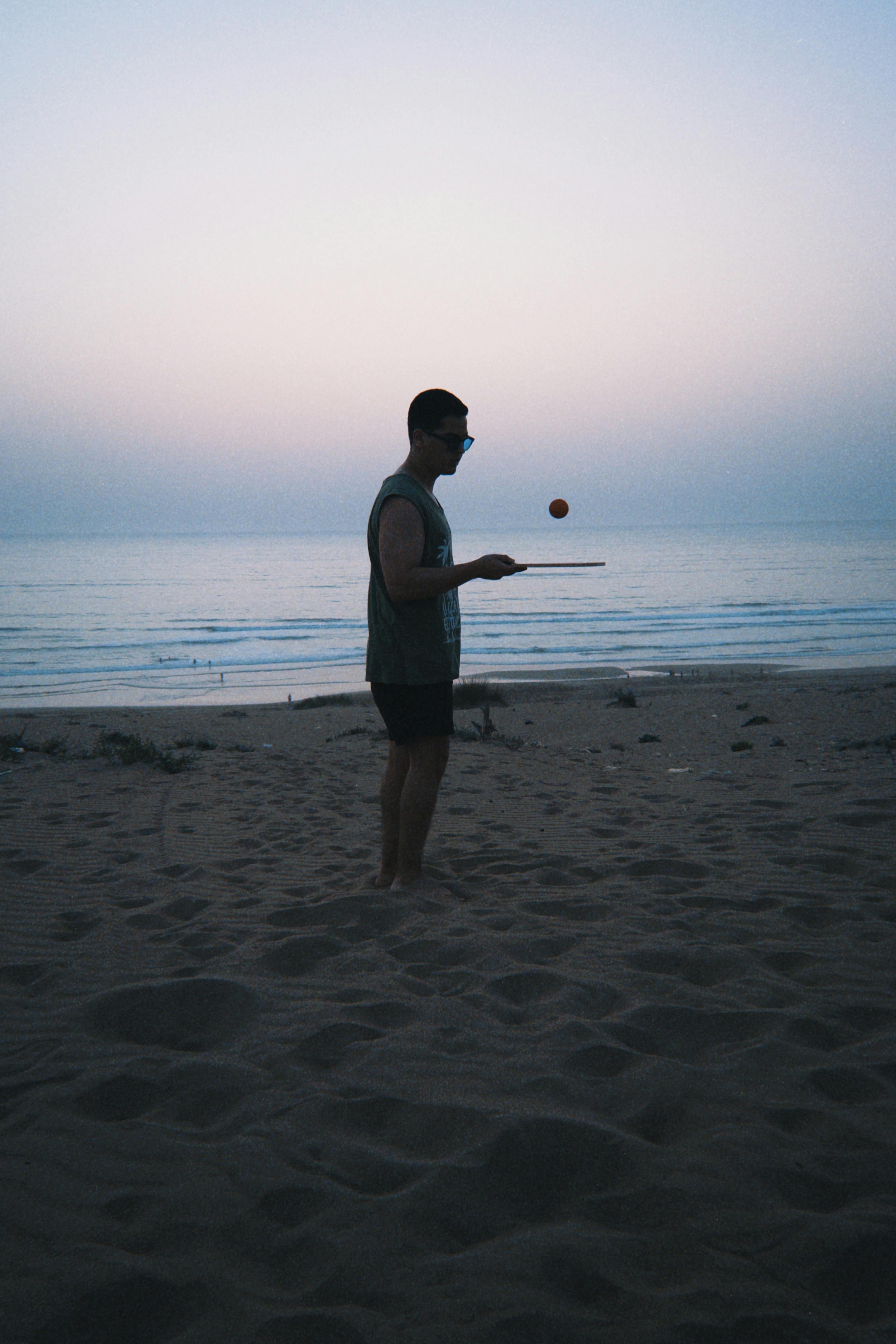 黄昏时分，一名男子在海滩上熟练地平衡球，捕捉到海边宁静的时刻